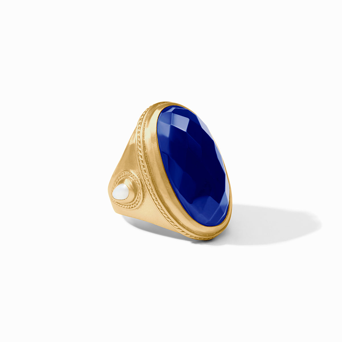 A gold signet ring featuring a large, faceted deep blue oval gemstone and a small white pearl accent on the band, set against a clean white background.
