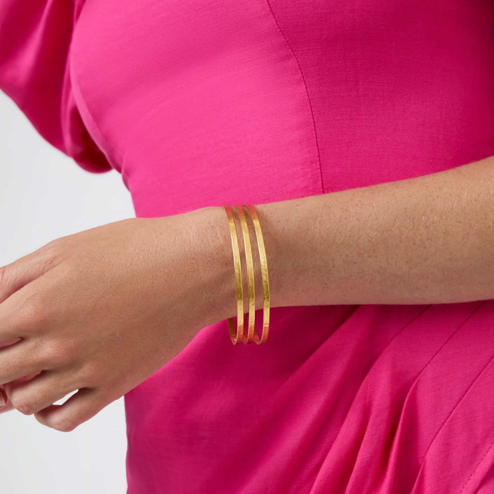 carousel; Model in pink dress wearing Crescent Bangle all gold in a stack of three