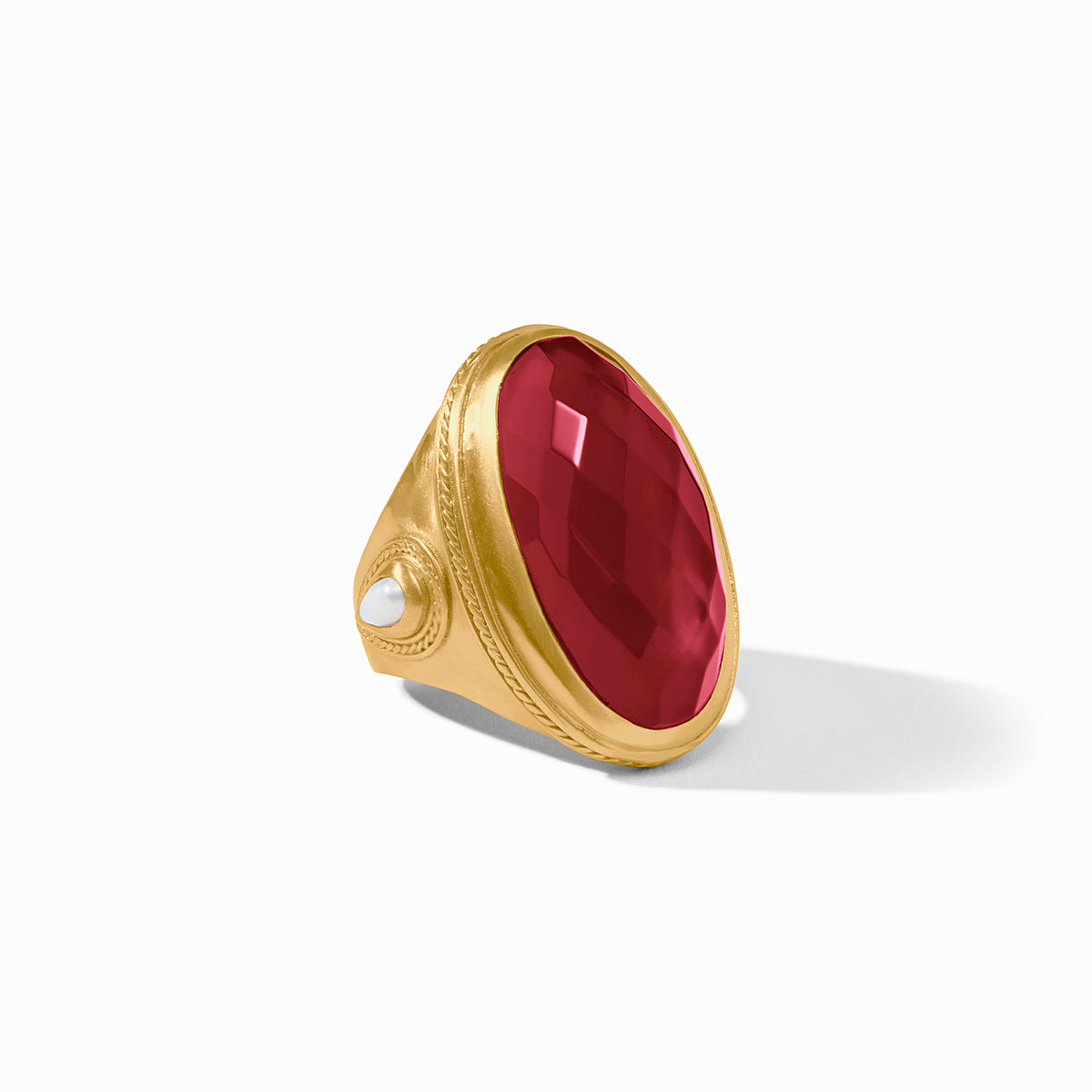 A gold signet ring featuring a large, faceted oval red gemstone and a small round white pearl on the band, set against a clean white background.