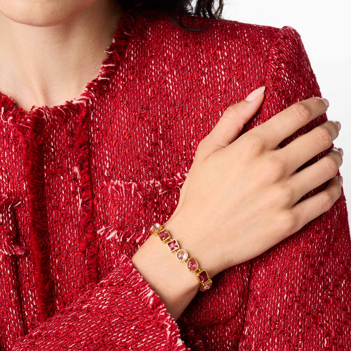 carousel, A close-up of a model wearing a gold bracelet with pink gemstones, paired with a textured red tweed jacket against a white background.